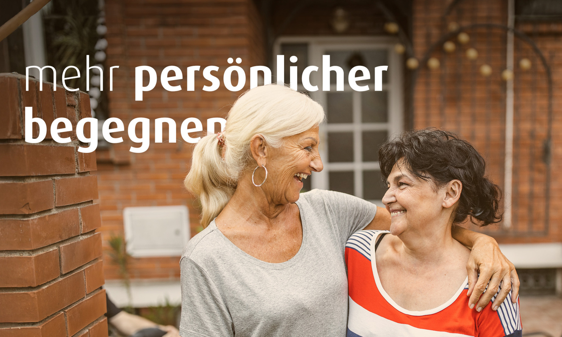 Zwei Frauen stehen nebeneinander und halten sich im Arm. Auf dem Bild steht der Text "mehr persönlicher begegnen".