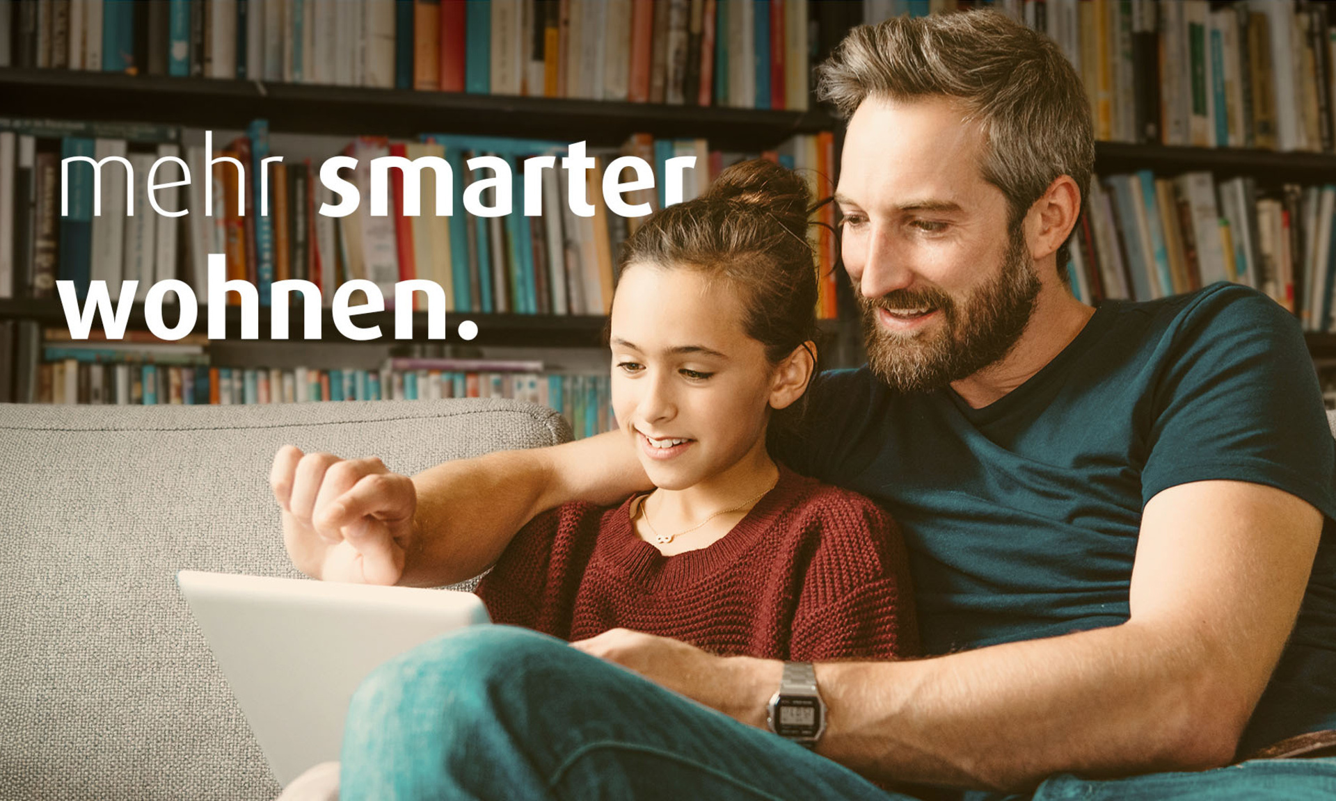 Ein Mann und ein Mädchen sitzen auf dem Sofa. Sie schauen zusammen auf ein Tablet. Auf dem Bild steht der Text "mehr smarter wohnen".