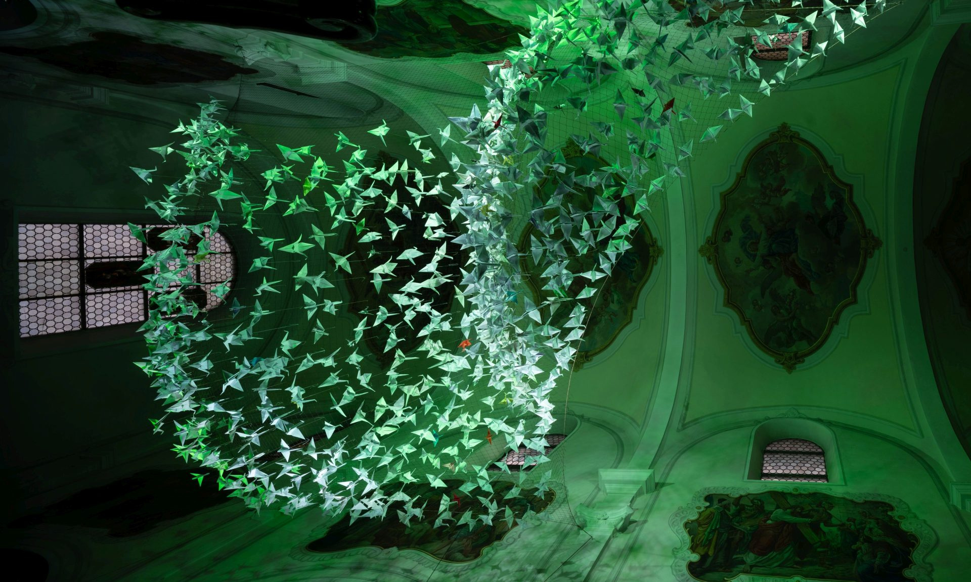 Blick nach oben in der Kelsterbacher Herz-Jesu-Kirche auf 843 Origami-Kraniche - hier grün illuminiert.