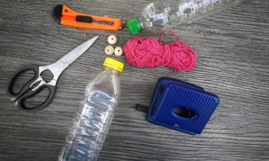 PET-Flaschen, Messer, Schere, Wolle, Locher und Holzperlen liegen auf einem Tisch.