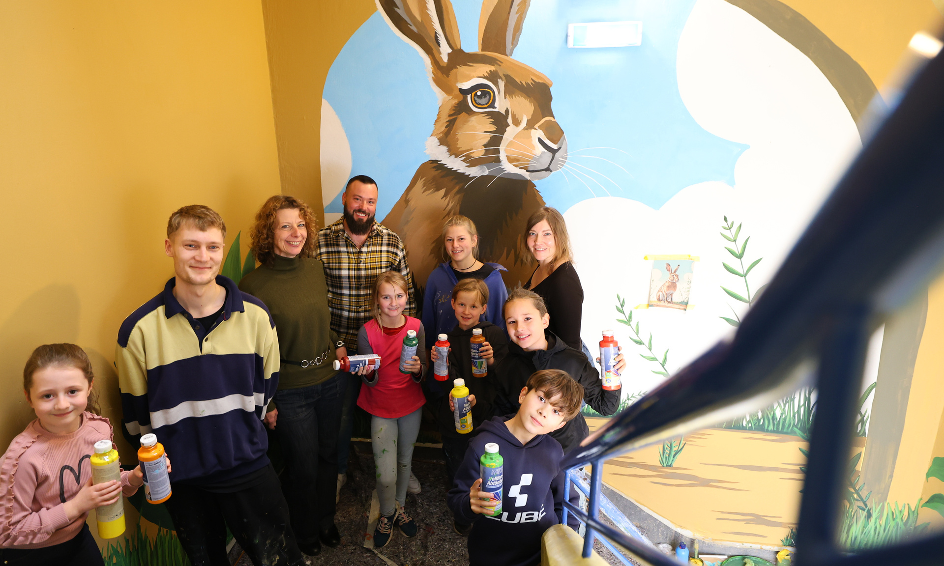 Eine Gruppe Kinder die stolz im Treppenhaus vor der bemalten Wand stehen