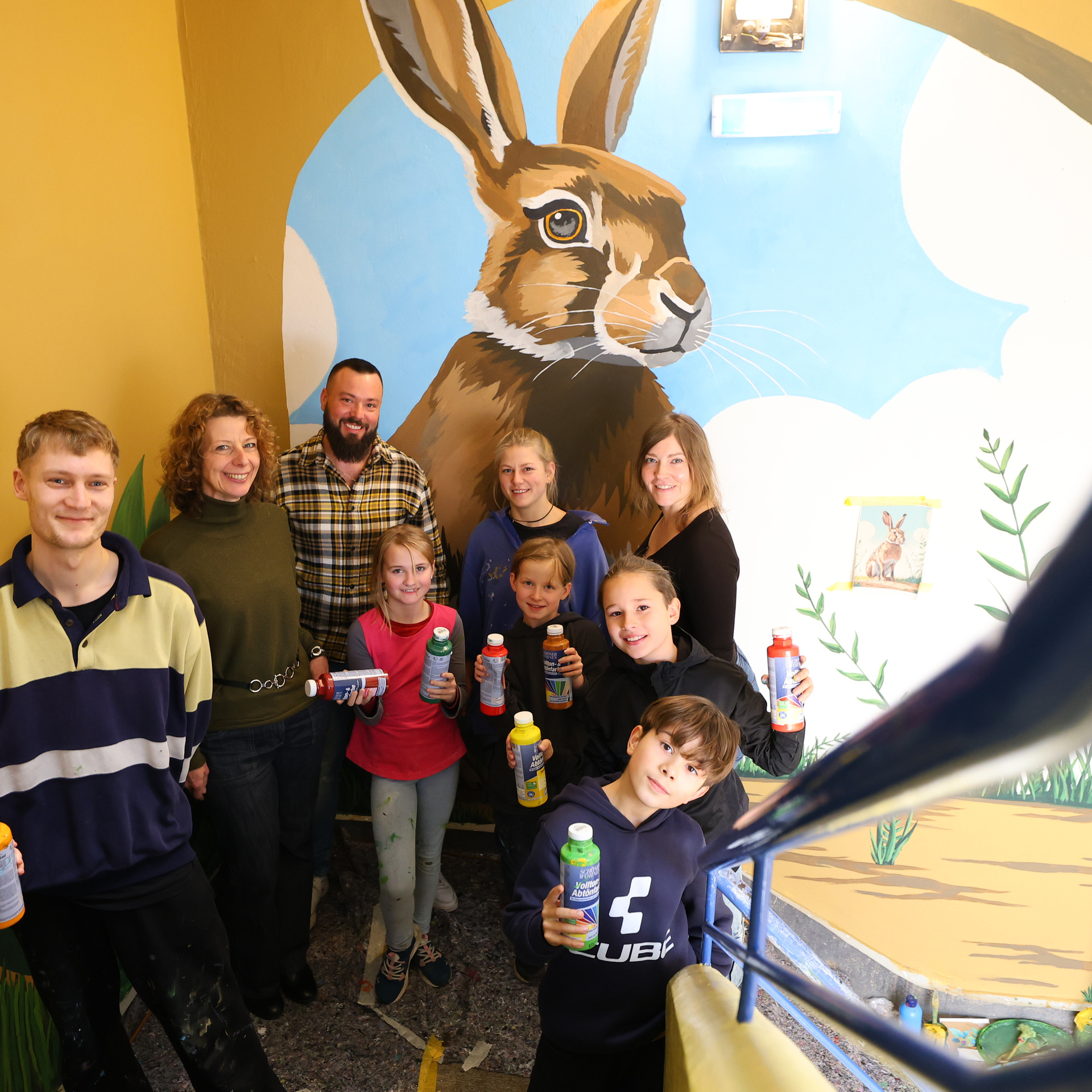 Eine Gruppe Kinder die stolz im Treppenhaus vor der bemalten Wand stehen