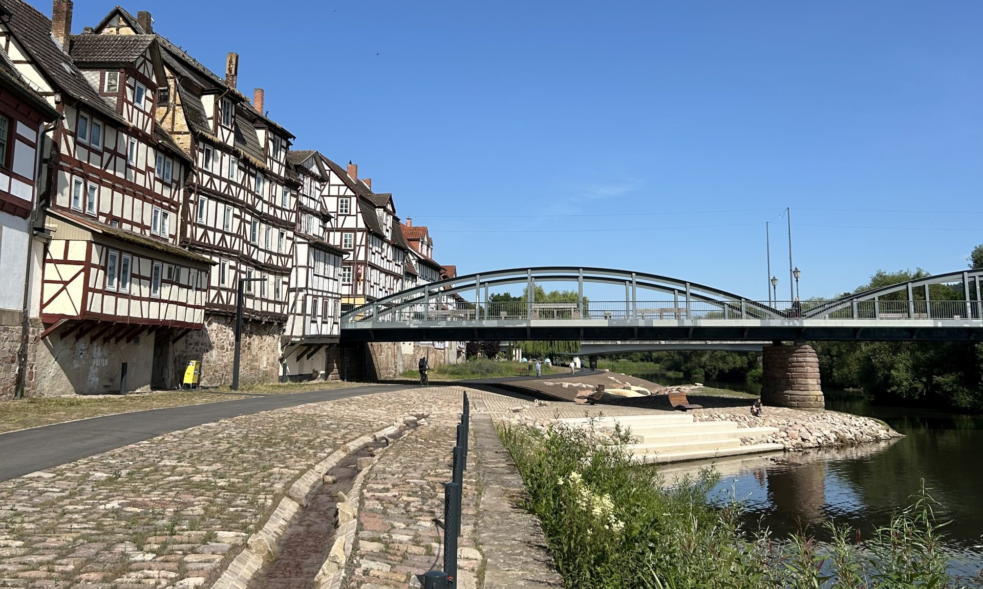 Neu gestalteter Uferbereich mit Bachlauf, rechts die Fulda, im Hintergrund Fachwerkhäuser und eine Brücke