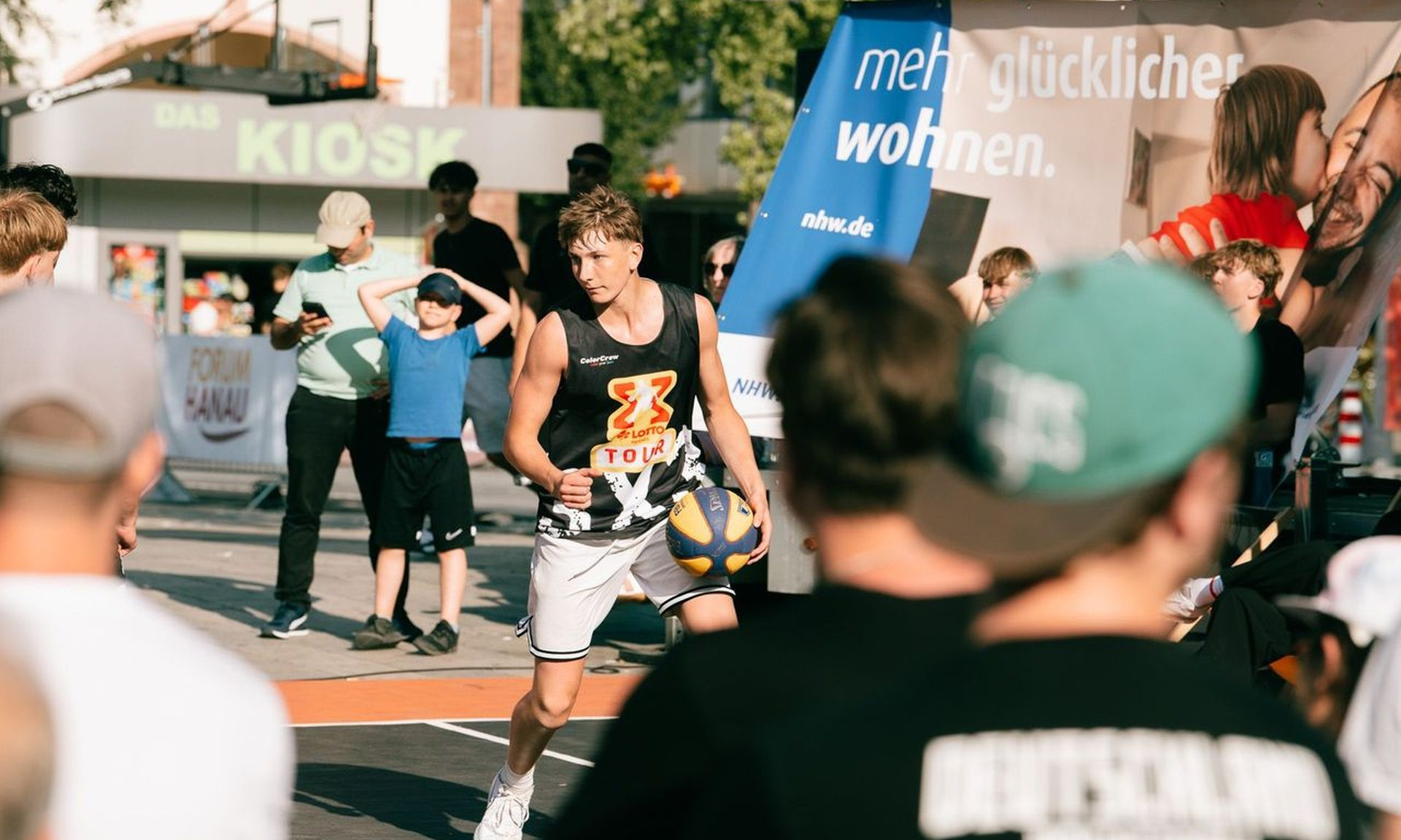 Streetbasketball-Spieler, rundherum Zuschauer, im Hintergrund das NHW-Plakat "mehr glücklicher wohnen"
