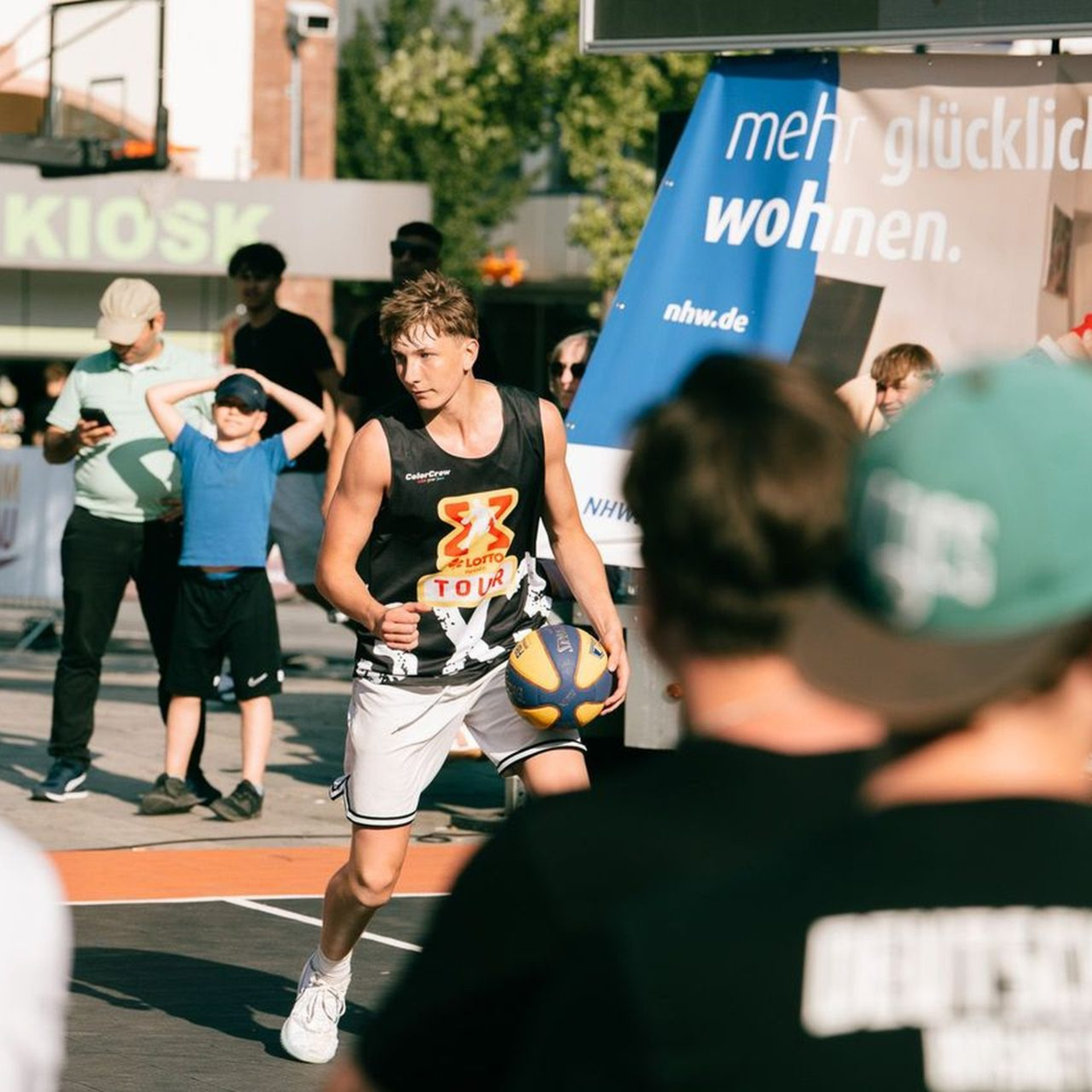 Streetbasketball-Spieler, rundherum Zuschauer, im Hintergrund das NHW-Plakat "mehr glücklicher wohnen"