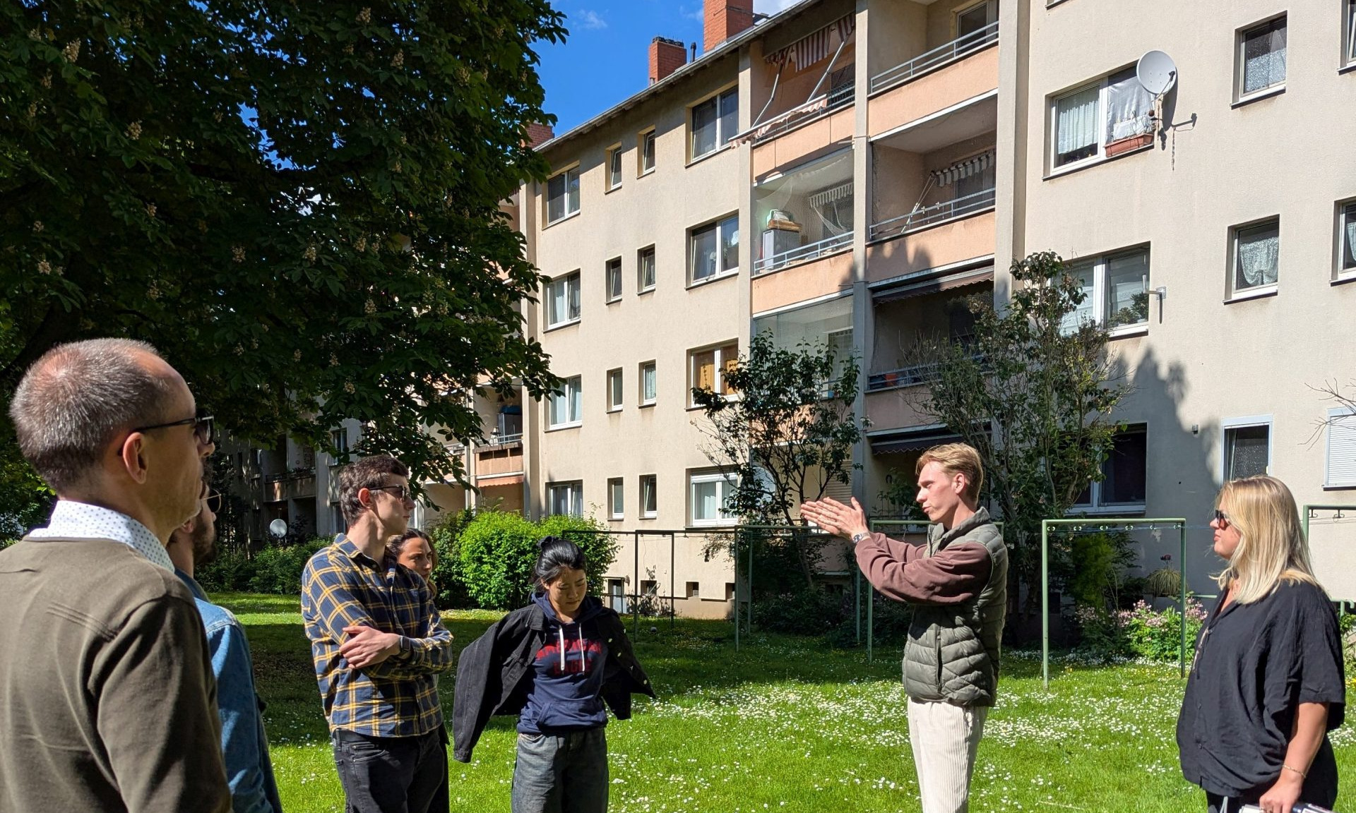 Mehrere Studierende auf der Grünfläche vor einem Mehrfamilienhaus