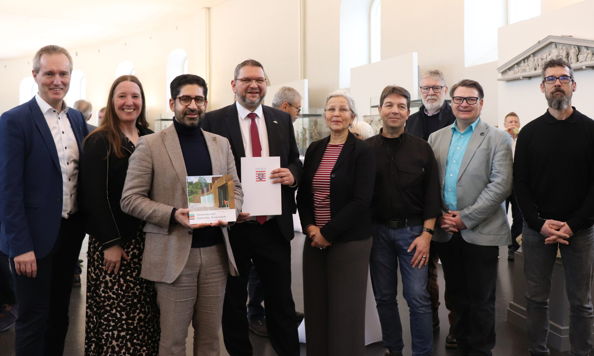 Minister Kaweh Mansoori übergibt den Förderbescheid an Bad Arolsens Bürgermeister Marko Lambion, beide sind umringt von weiteren Personen