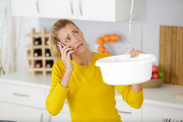 Frau telefoniert und hält eine Schüssel in der Hand. Von oben läuft Wasser in die Schüssel.