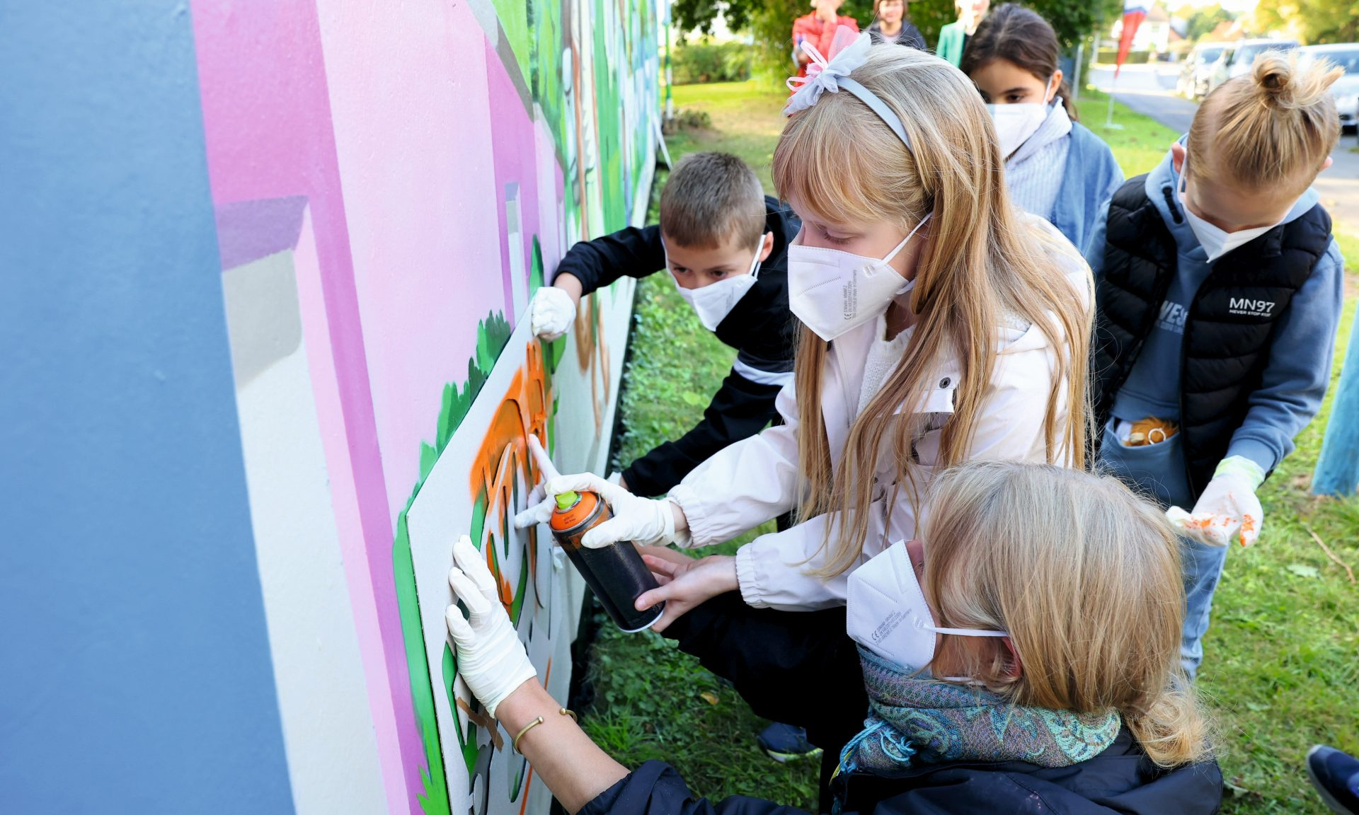 Mit Sprühflasche, Mundschutz und Handschuhen: Schüler:innen der Grundschule Waldau verwandeln unter Regie der Künstler Sander Bartel und Dana Bormann die Garagenrückwand in ein buntes Kunstwerk.