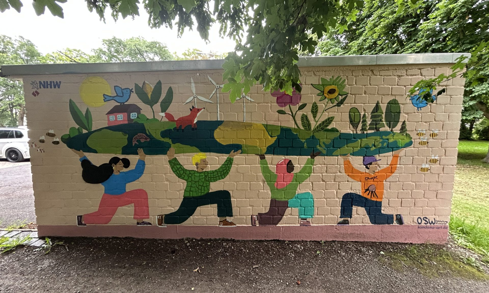 Buntes Gemälde auf einer Garagenwand: Vier Jugendliche halten etwas in ihren Händen, das die Welt in Scheibenform sein könnte, mit Sonne, Windrädern, Blumen und Tieren. Das Thema ist Nachhaltigkeit.