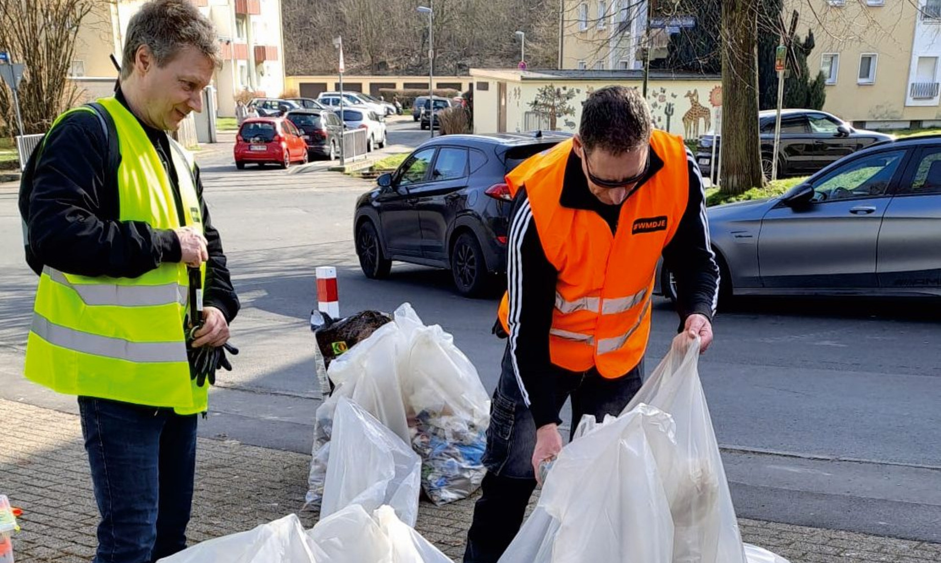 Zwei Männer in Warnwesten mit mehreren großen und gut gefüllten Müllsäcken