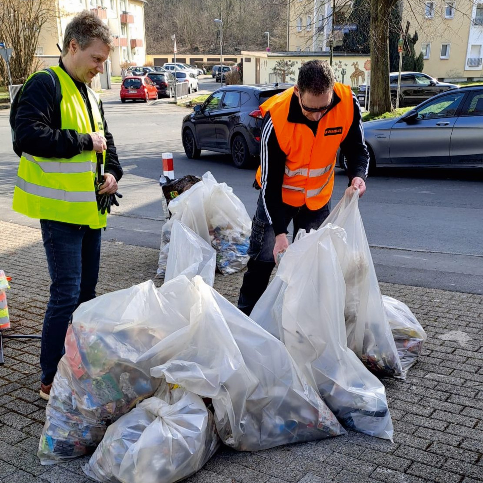 Zwei Männer in Warnwesten mit mehreren großen und gut gefüllten Müllsäcken