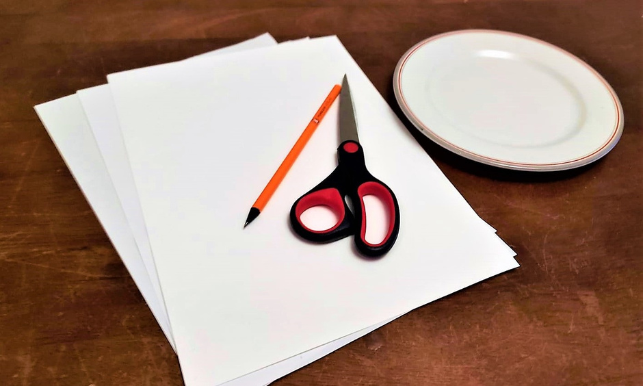 Papier, Stift, Schere und Teller liegen auf einem Tisch.