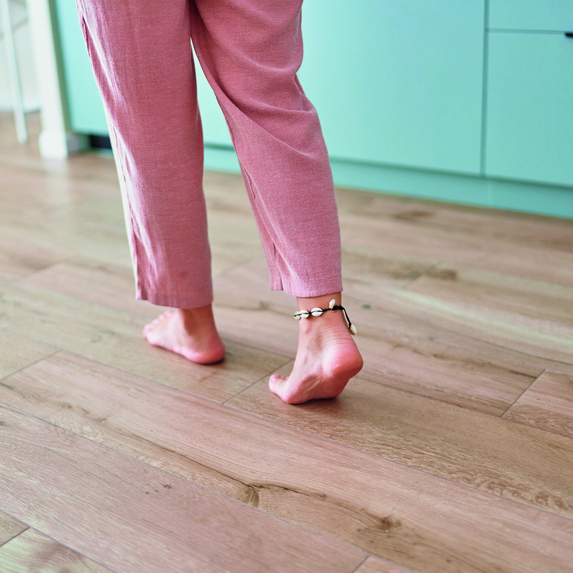 Frau läuft barfuß über einen Parkettboden. Oberkörper ist abgeschnitten. Fokus auf den Boden.