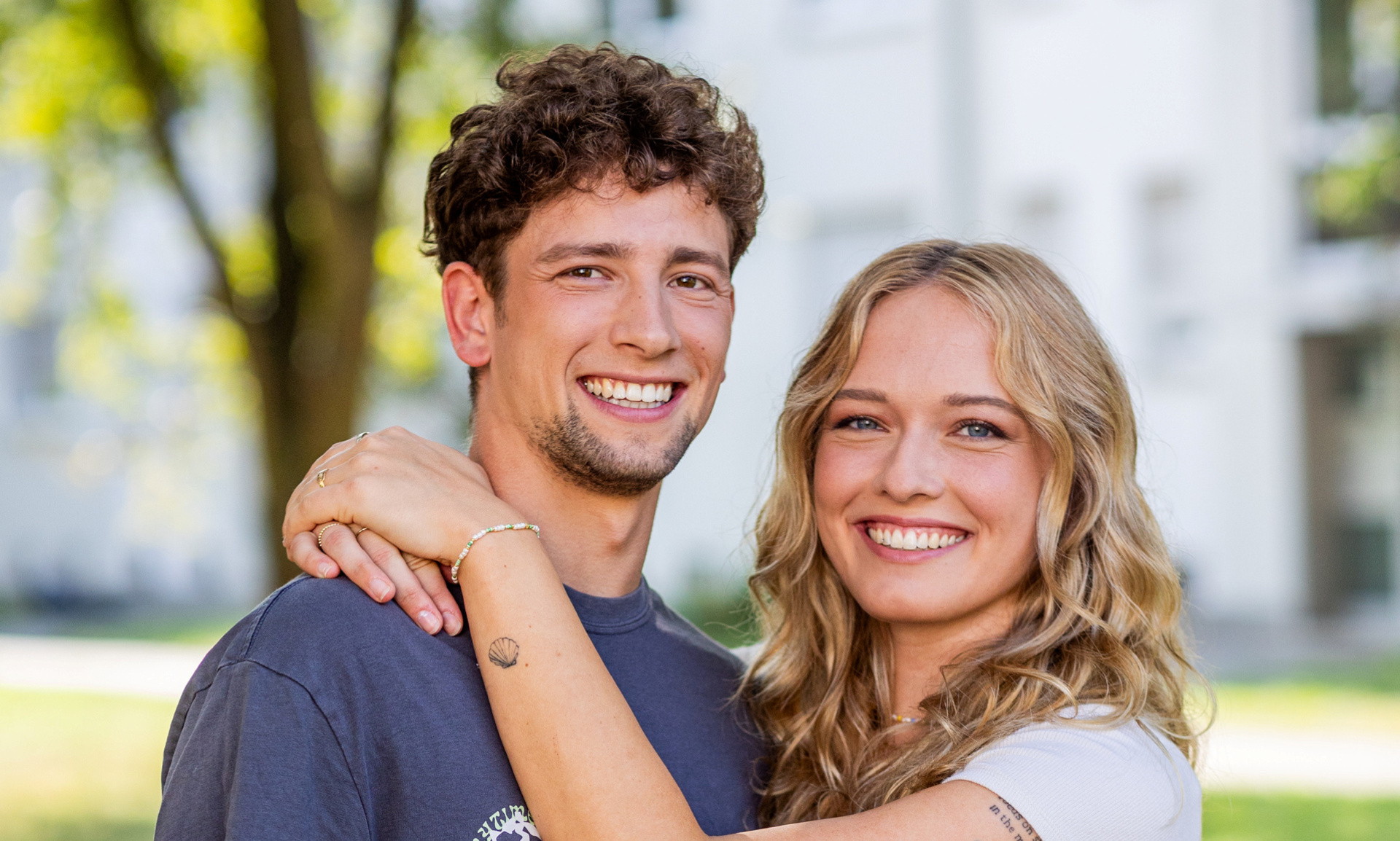 Frau umarmt Mann. Im Hintergrund sieht man ein Haus.