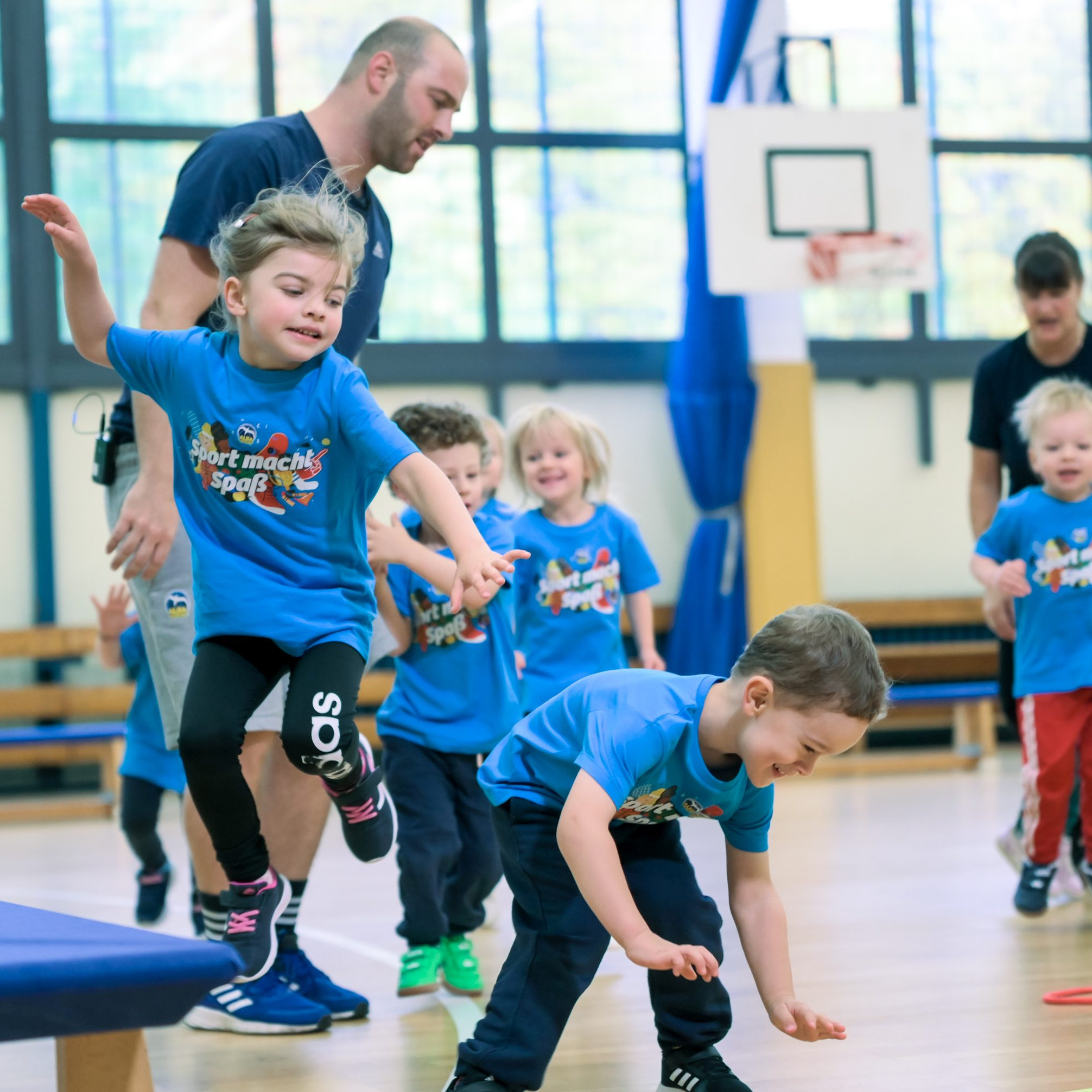 Mehrere Kinder in blauen T-Shirts beim Turnen in einer Turnhalle