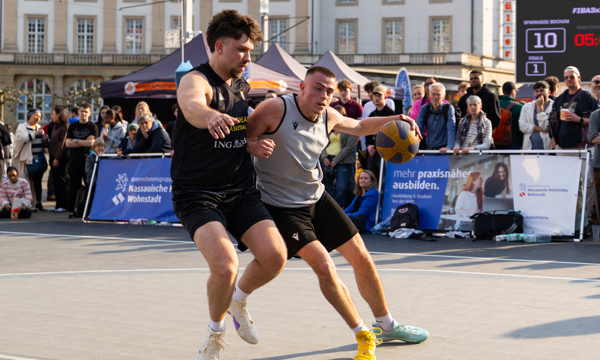 Zwei junge Männer im Zweikampf mit dem Ball unter dem Basketballkorb.