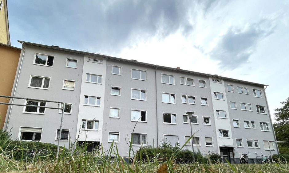 Ein Wohnhaus in verschiedenen Beigetönen vor bewölktem Himmel.