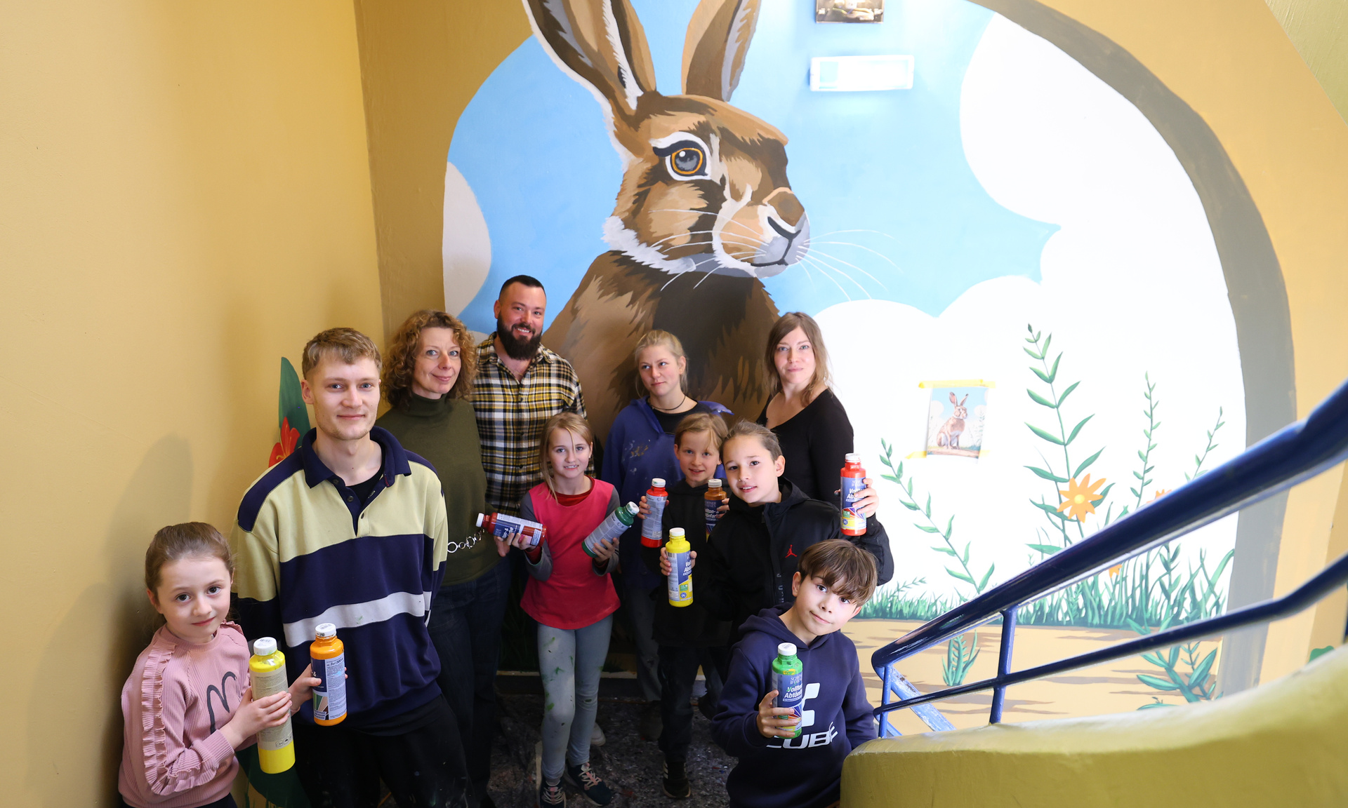 Gruppe von Kindern und Jugendlichen steht in einem Treppenhaus mit Farbflaschen in der Hand. Im Hintergrund ist gemaltes Wandbild mit einem Hasen.