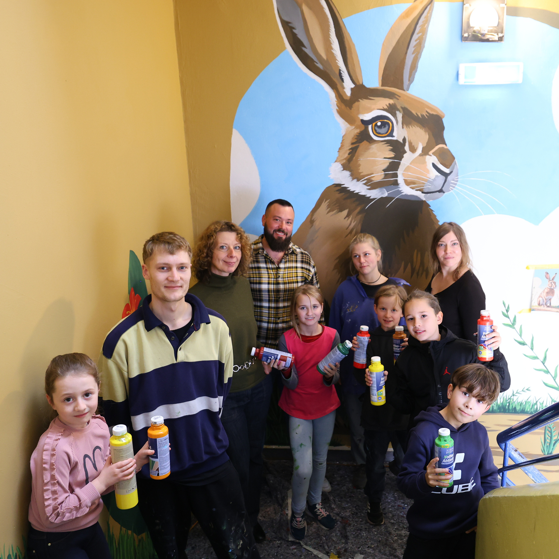 Gruppe von Kindern und Jugendlichen steht in einem Treppenhaus mit Farbflaschen in der Hand. Im Hintergrund ist gemaltes Wandbild mit einem Hasen.