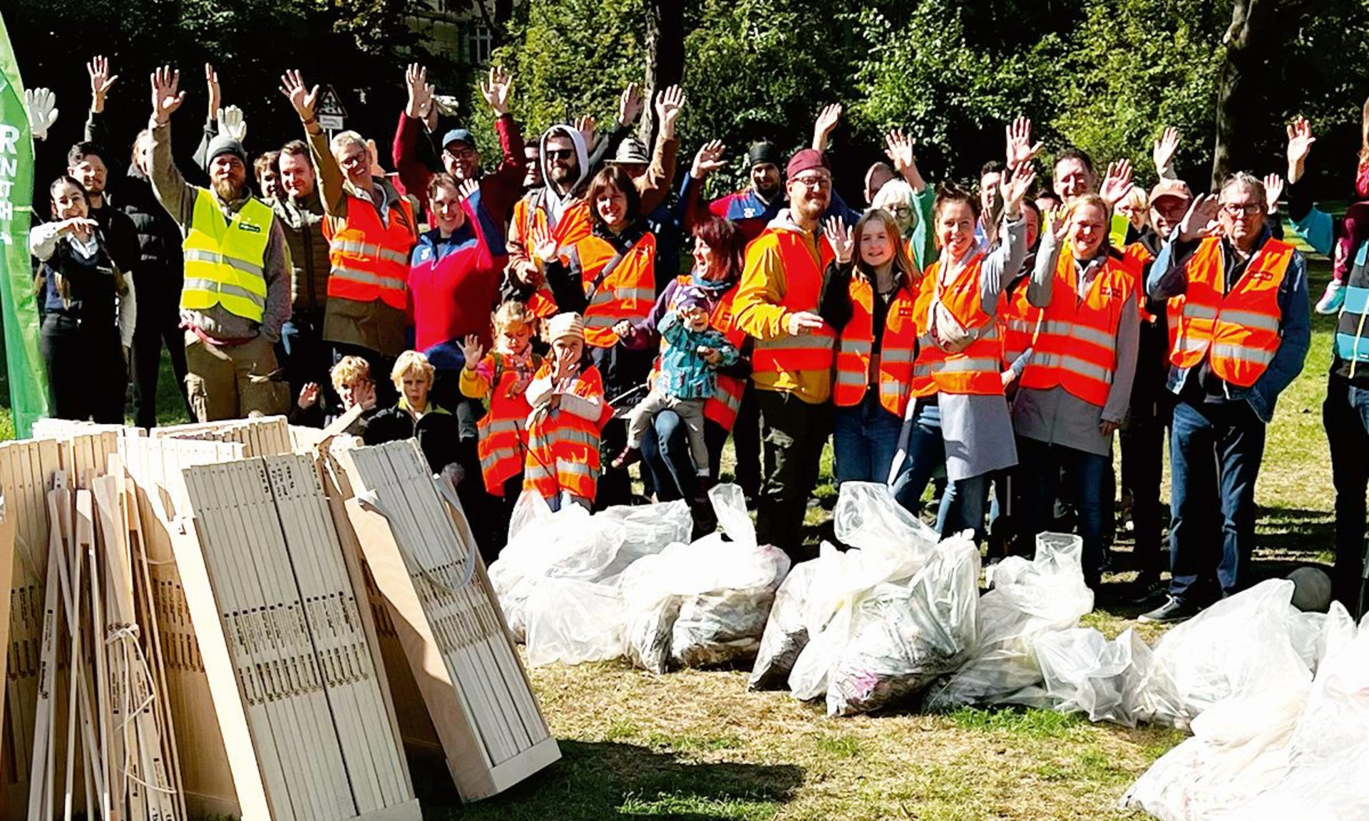 Eine große Gruppe von Menschen in Warnwesten mit vielen Müllsäcken winken gut gelaunt Richtung Kamera