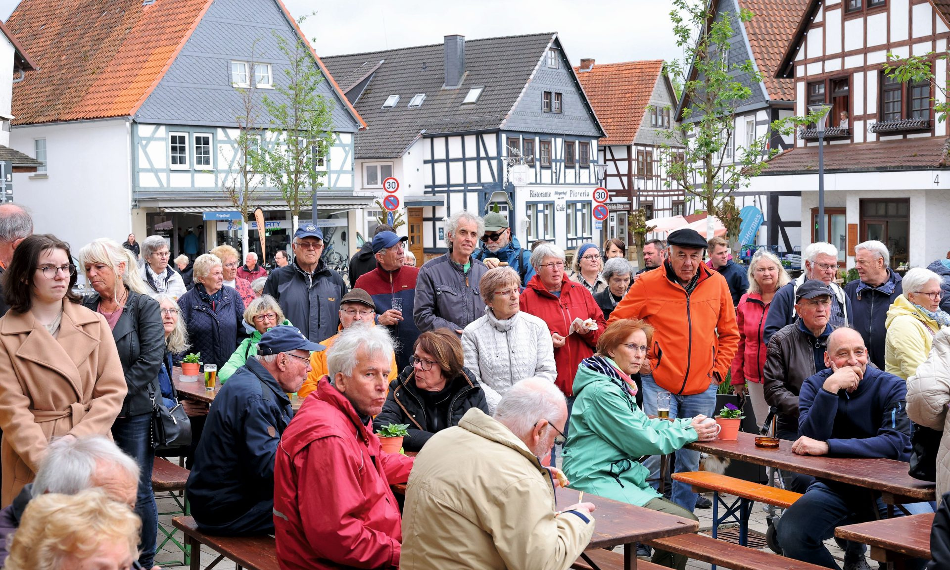 Viele Menschen sitzen auf Bänken und an Tischen vor historischer Fachwerkkulisse