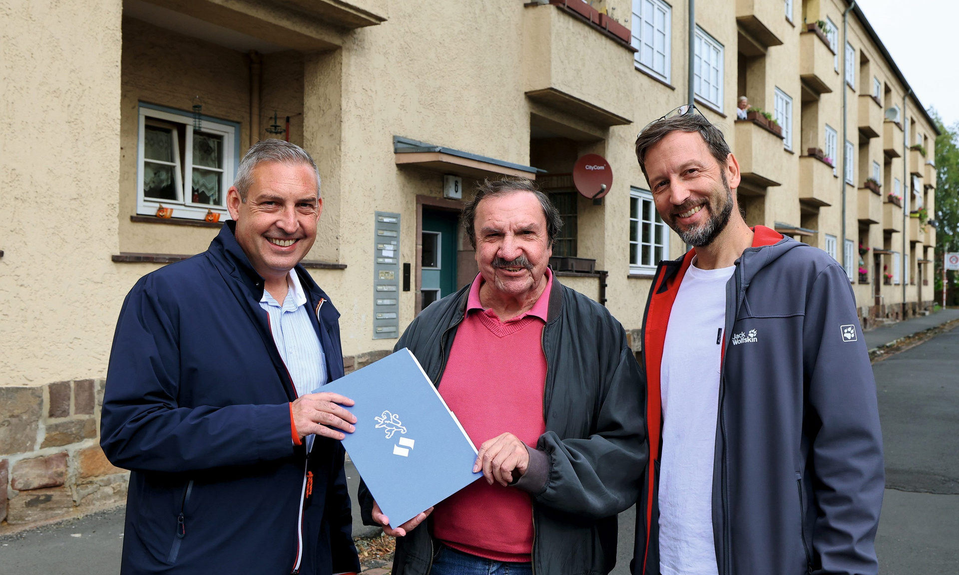 NHW-Regionalcenterleiter Sascha Holstein (li.) und Markus Beecht, Geschäftsführer der Evangelischen Wohnraumhilfe (re.), übergeben die Wohnung an Burgfried Göbel.