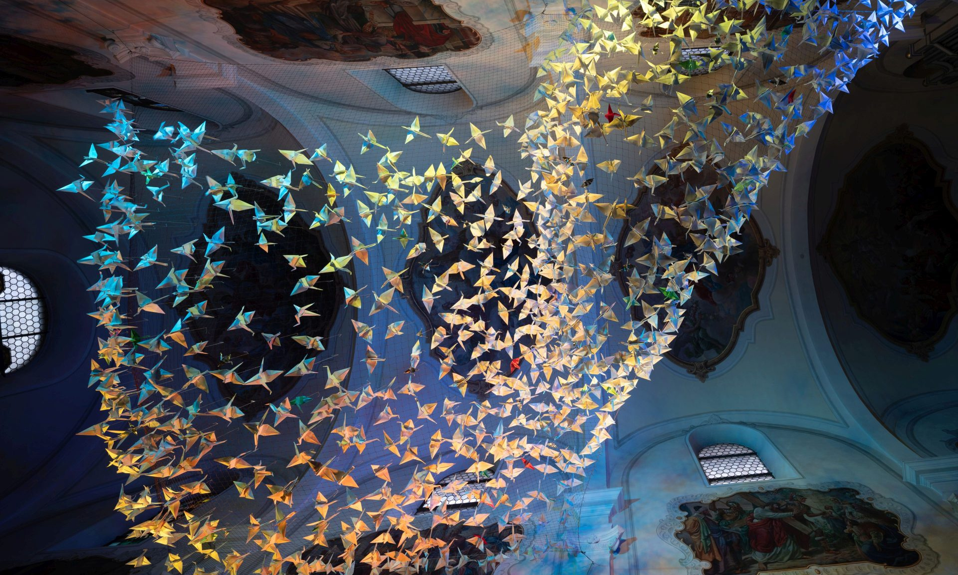 Blick nach oben in der Kelsterbacher Herz-Jesu-Kirche auf 843 Origami-Kraniche - hier golden illuminiert.