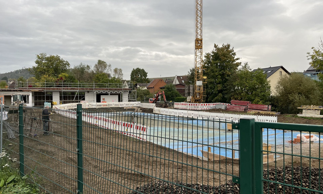 Blick auf das Freibad von Großen-Buseck mit Gerüst und Baustellenabsperrungen, im Vordergrund ein grüner Zaun, im Hintergrund ein Kran