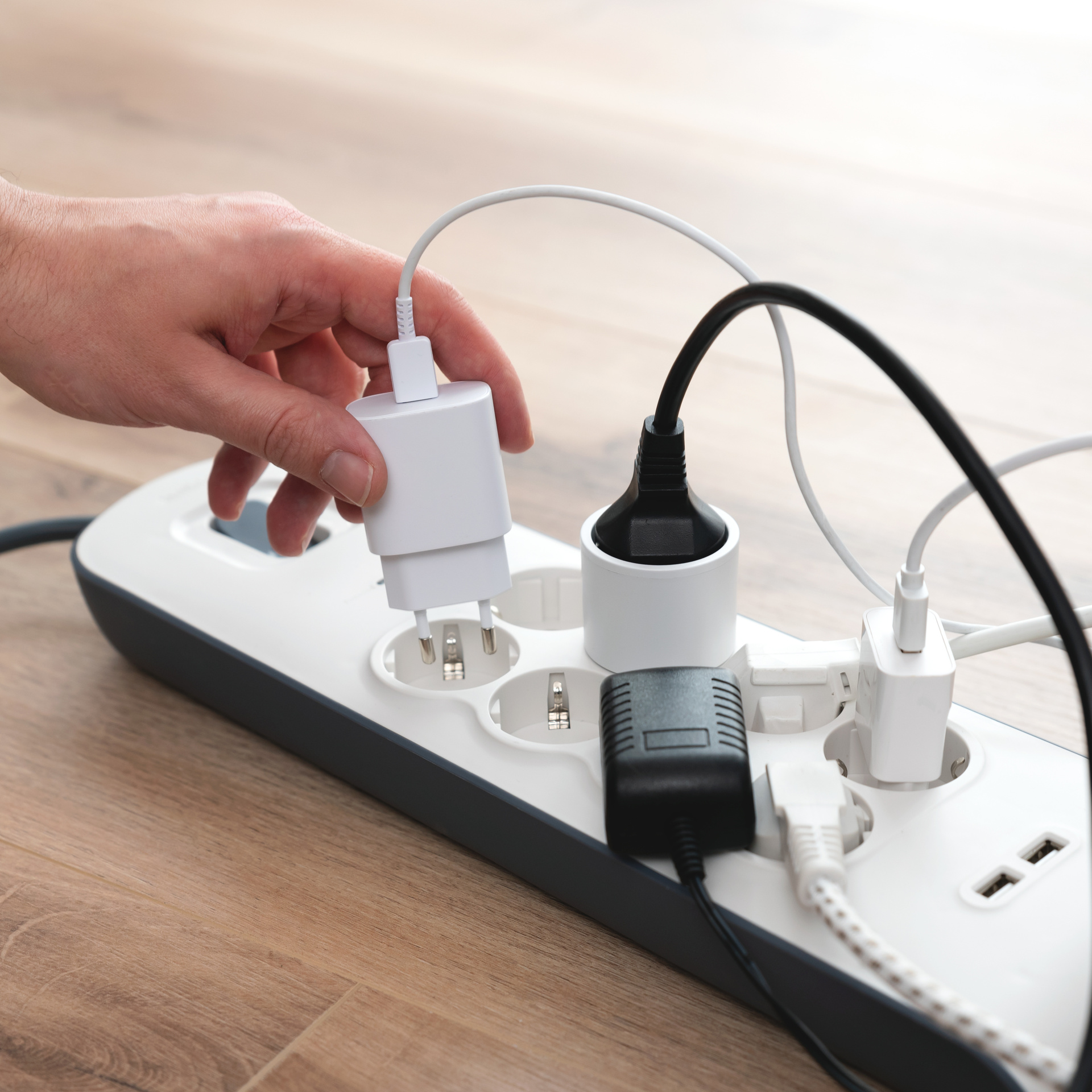 Steckdosenleiste mit Stromsteckern und einer Hand die ein weiteres Kabel einsteckt