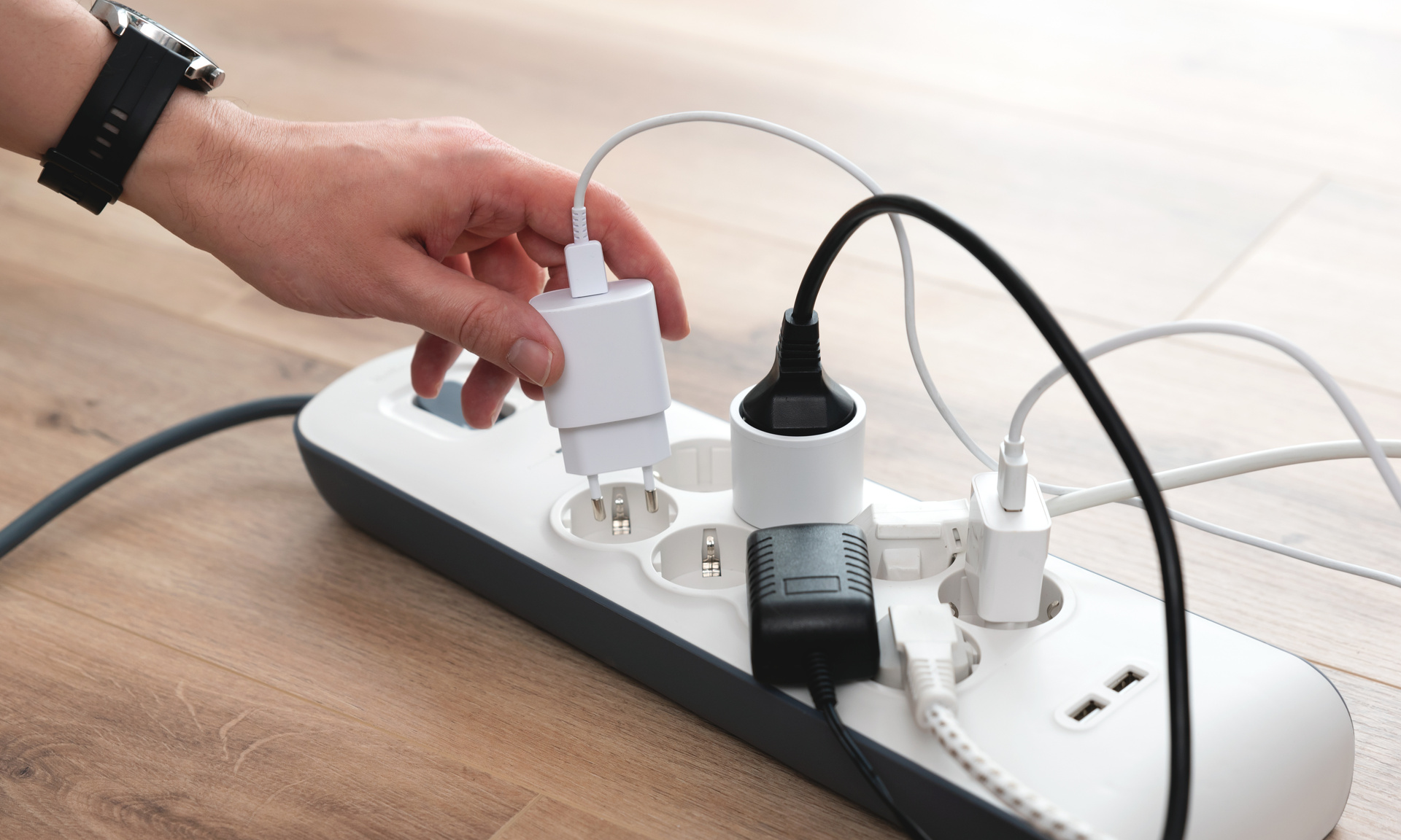 Steckdosenleiste mit Stromsteckern und einer Hand die ein weiteres Kabel einsteckt