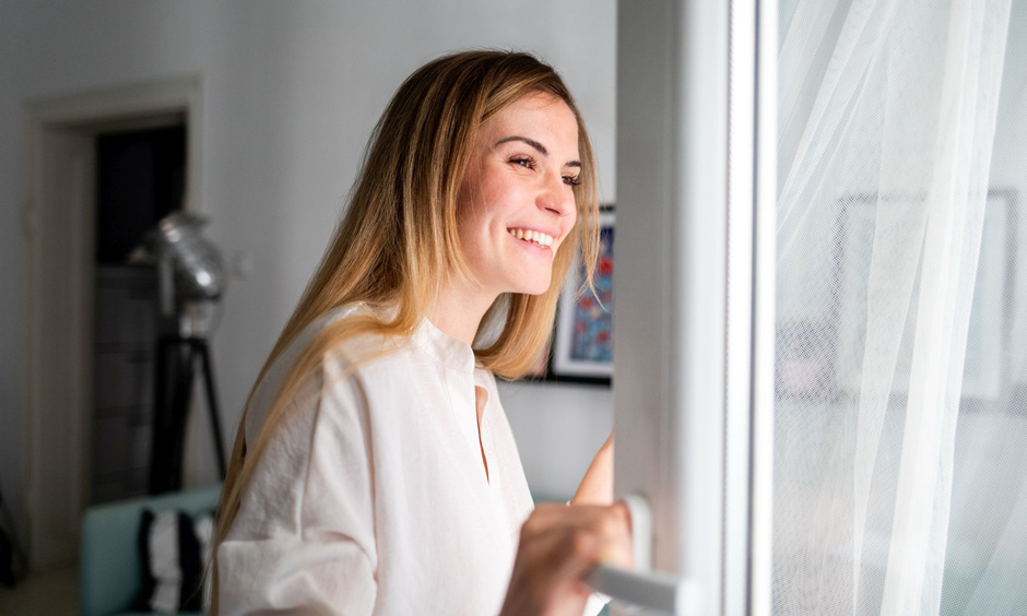 Frau öffnet das Fenster und schaut lächelnd nach draussen.