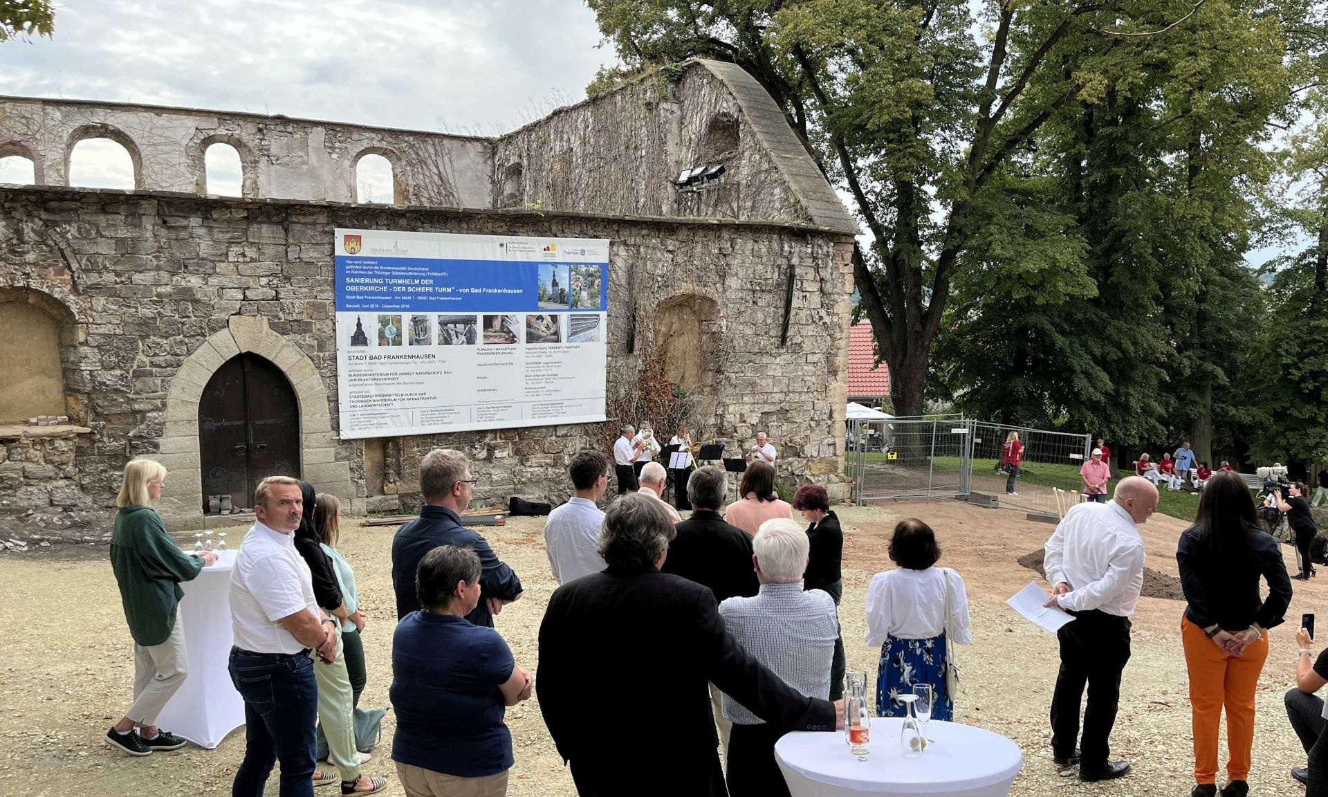 Gruppe von Menschen vor dem alten Kirchenschiff, an dem eine Infotafel hängt