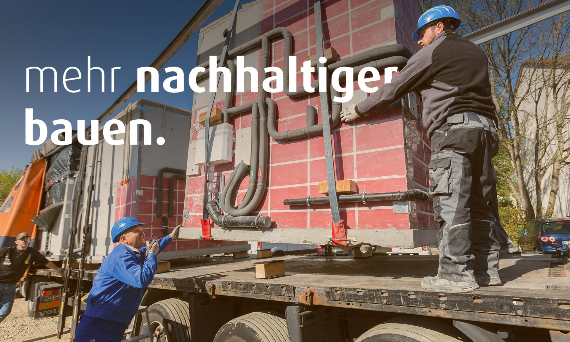 Zwei Männer in Baustellenkleidung entladen einen Lastwagen, der ein Modul für die Baustelle angeliefert hat. Auf dem Bild steht der Text "mehr nachhaltiger bauen".