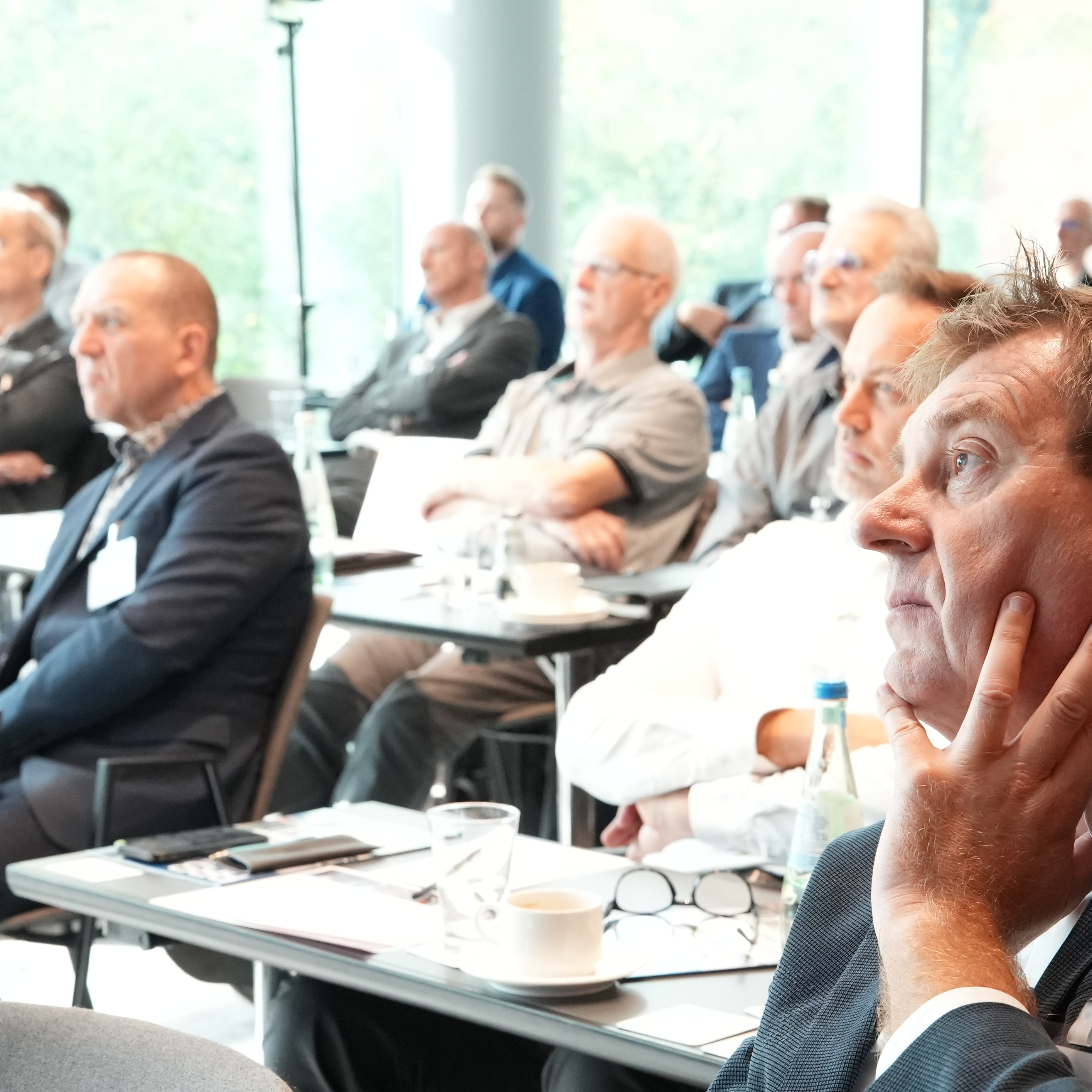 Eine Gruppe von Menschen sitzt an Tischen und hört dem aktuellen Redner beim BundesBauBlatt-Gipfel aufmerksam zu.
