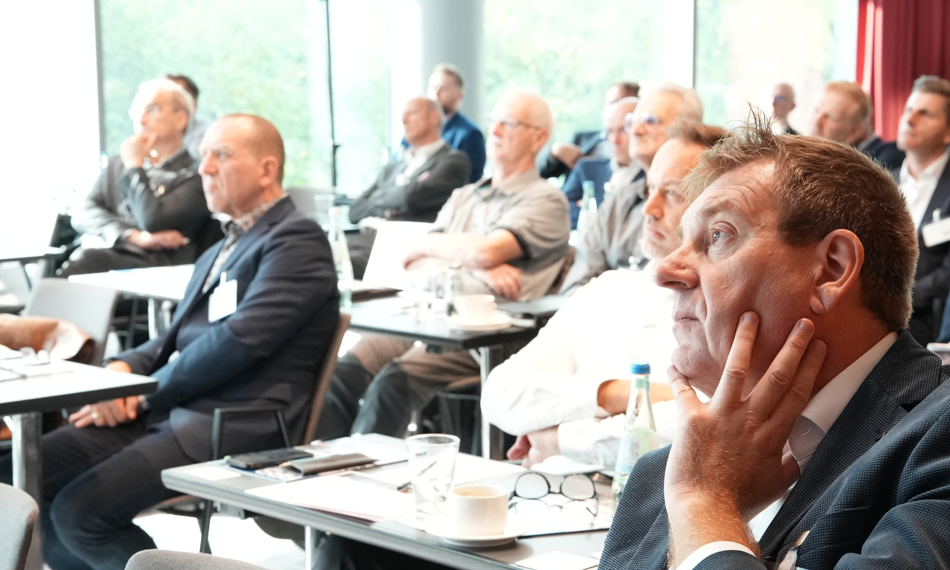 Eine Gruppe von Menschen sitzt an Tischen und hört dem aktuellen Redner beim BundesBauBlatt-Gipfel aufmerksam zu.