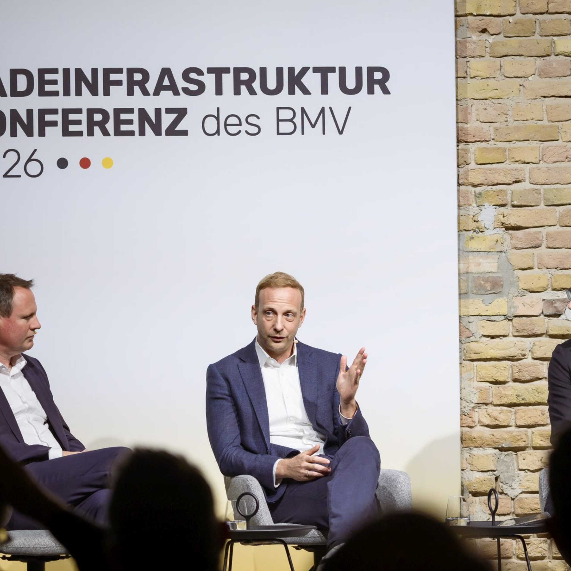 Drei Männer bei einer Podiumsdiskussion, hinter ihnen der Schriftzug "Ladeinfrastrukturkonferenz"
