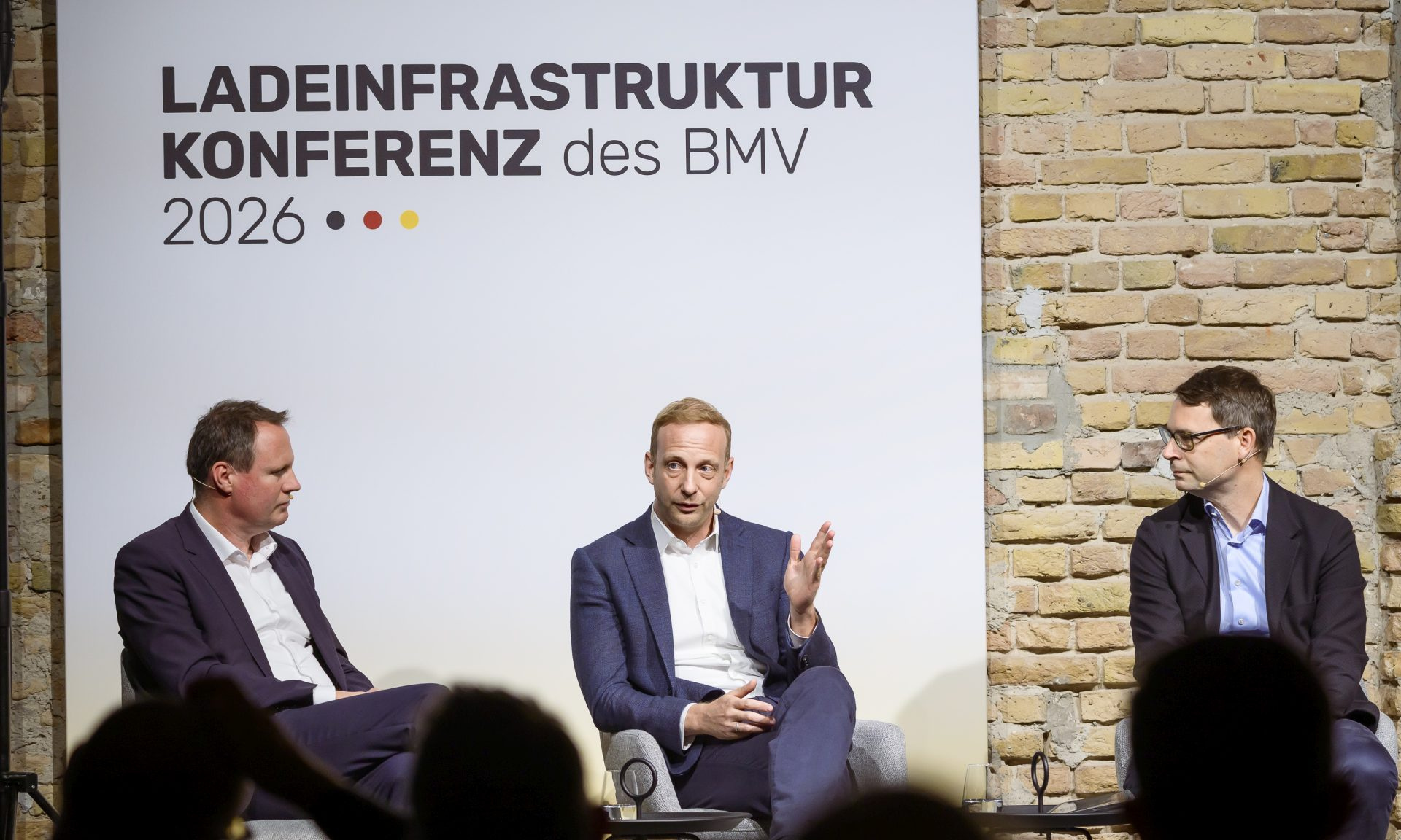 Drei Männer bei einer Podiumsdiskussion, hinter ihnen der Schriftzug "Ladeinfrastrukturkonferenz"