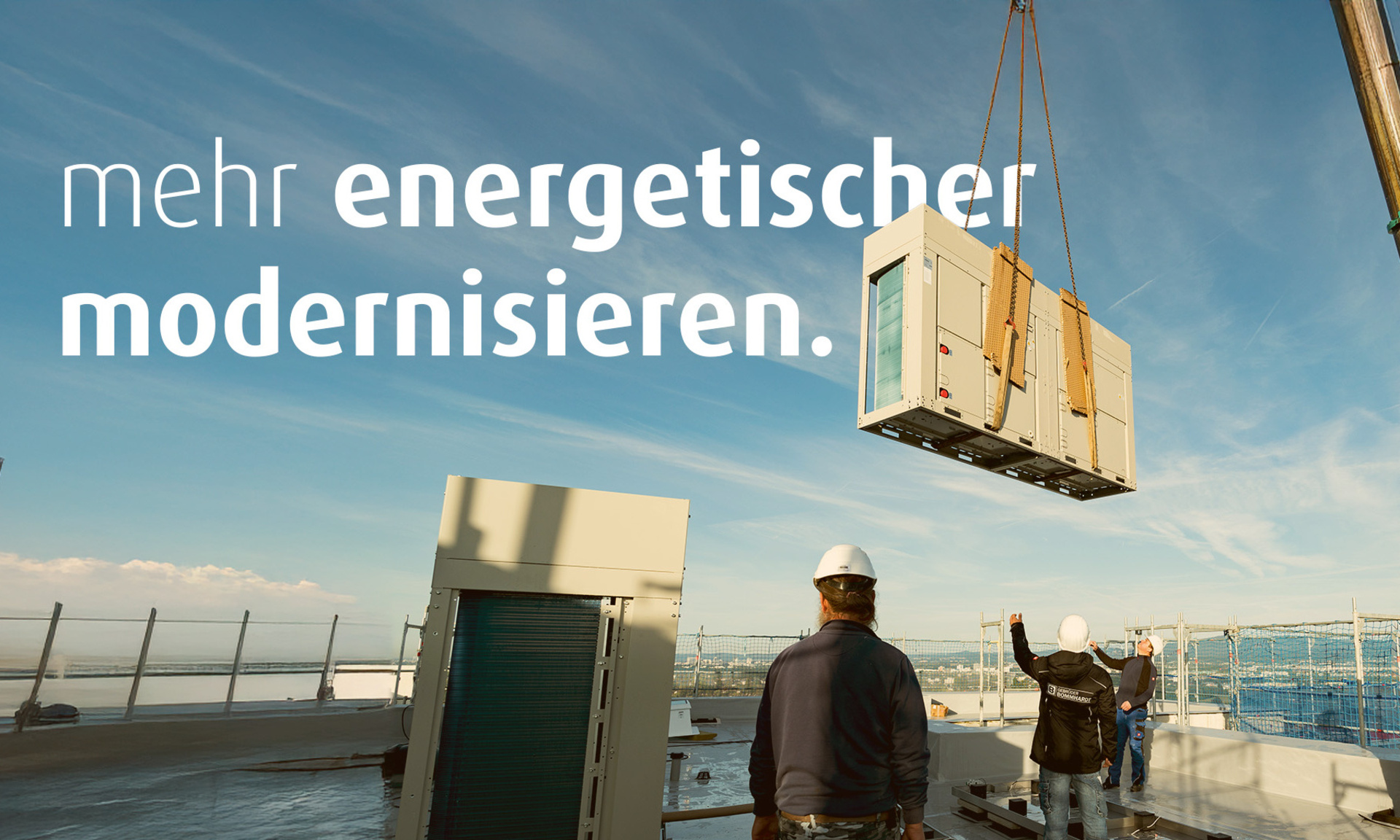Mit einem Kran wird eine Wärmepumpe auf ein Hausdach gehoben. Vier Bauarbeiter stehen auf dem Dach. Auf dem Bild steht der Text "mehr energetischer modernisieren".