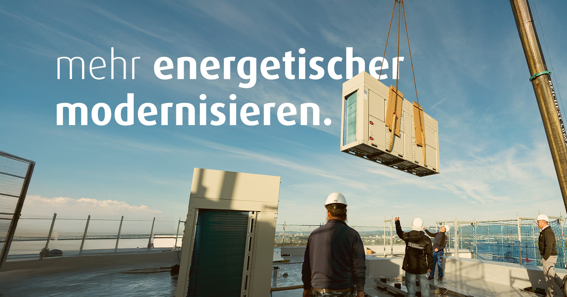 Mit einem Kran wird eine Wärmepumpe auf ein Hausdach gehoben. Vier Bauarbeiter stehen auf dem Dach. Auf dem Bild steht der Text "mehr energetischer modernisieren".