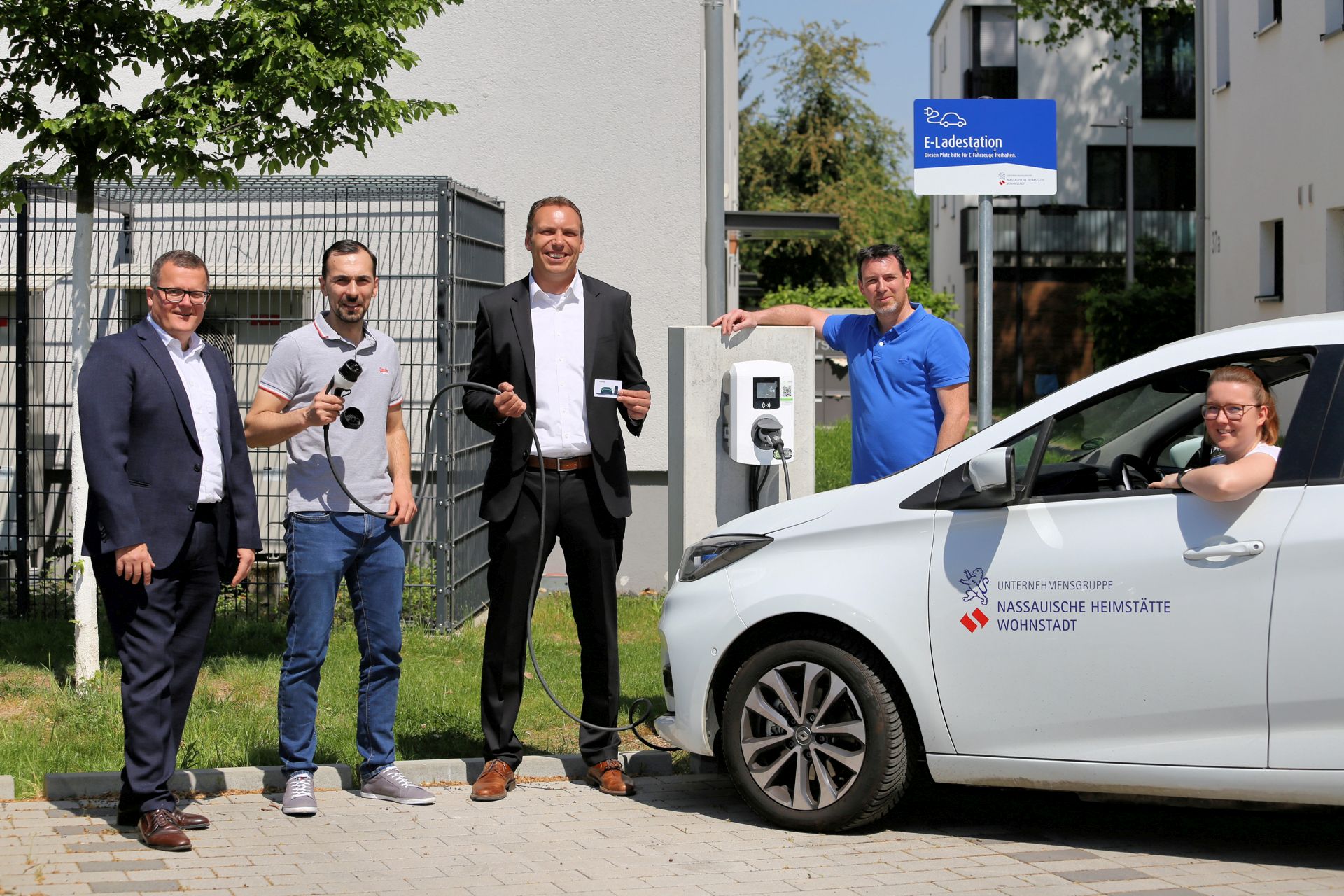 Drei Männer neben Auto, ein Mann hinter Auto, eine Frau in Auto