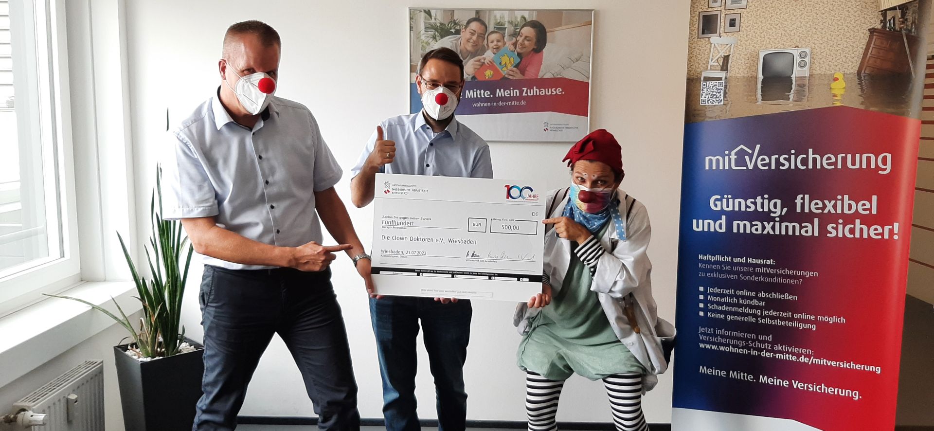 Zwei Männer übergeben einen Scheck an einen Clown