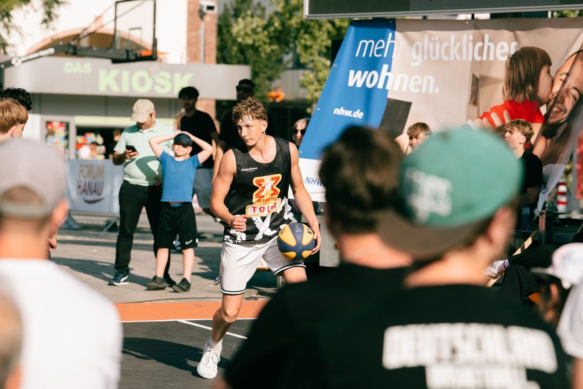 Streetbasketball-Spieler, rundherum Zuschauer, im Hintergrund das NHW-Plakat "mehr glücklicher wohnen"