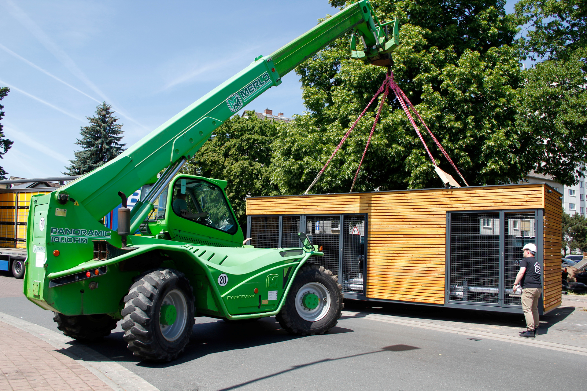 Ein grüner Teleskoplader hebt Energiemodul mit je sechs Luft-Wasser-Wärmepumpe an.