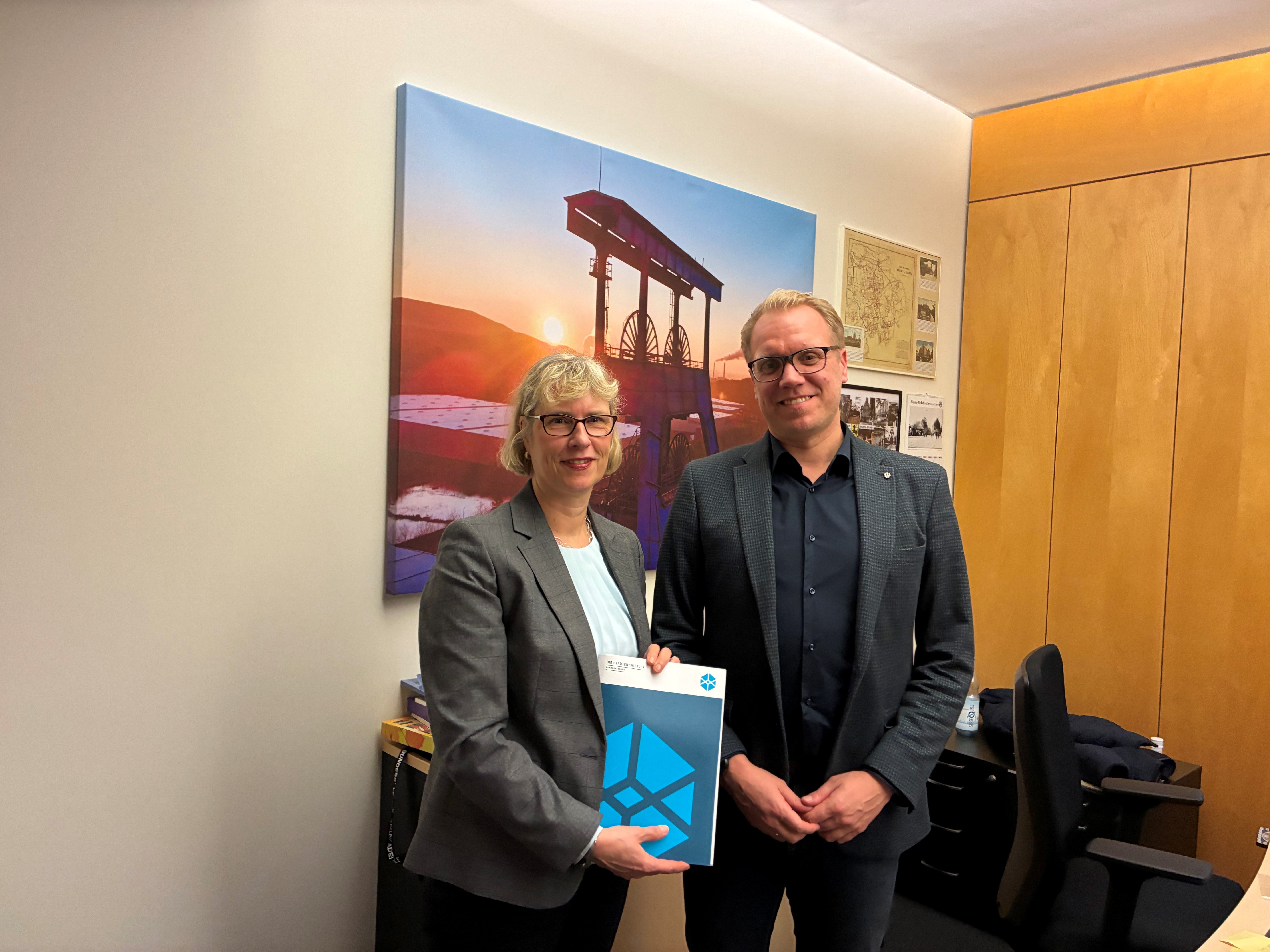Monika Fontaine-Kretschmer und Hendrik Bollmann stehen mit dem Empfehlungspapier posierend der Kamera zugewandt.